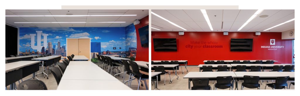 Classroom with red wall with media displays; other wall wrapped with a view of the downtown Indy skyline with a white trident.