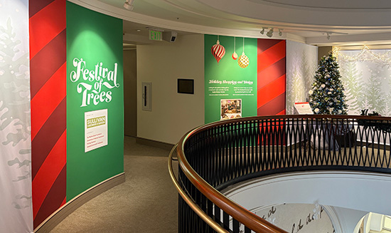 Curved walls decorated in red and green for Festival of trees are flanked by exhibit walls covered with temporary fabric decorated with trees